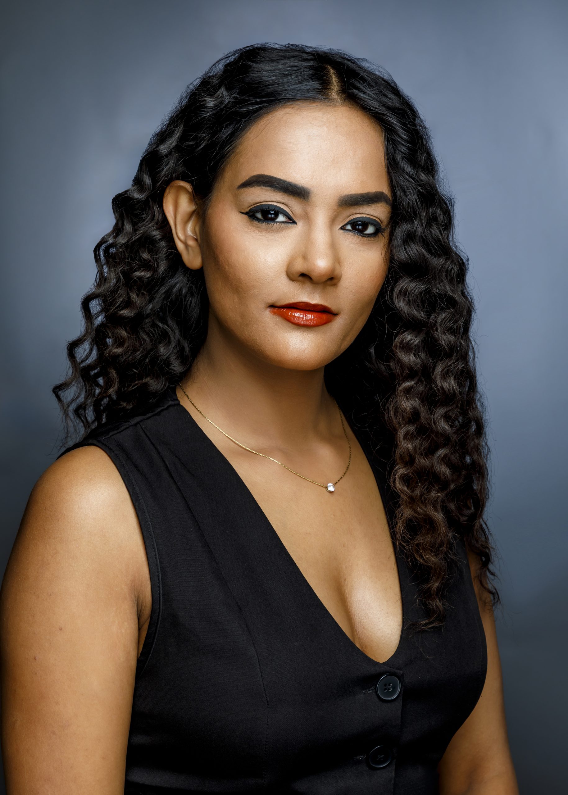 Professional portrait of a woman with dark curly hair against a blue studio background, taken by Marcos Appelt Portrait Photographer in Bristol and Southwest.