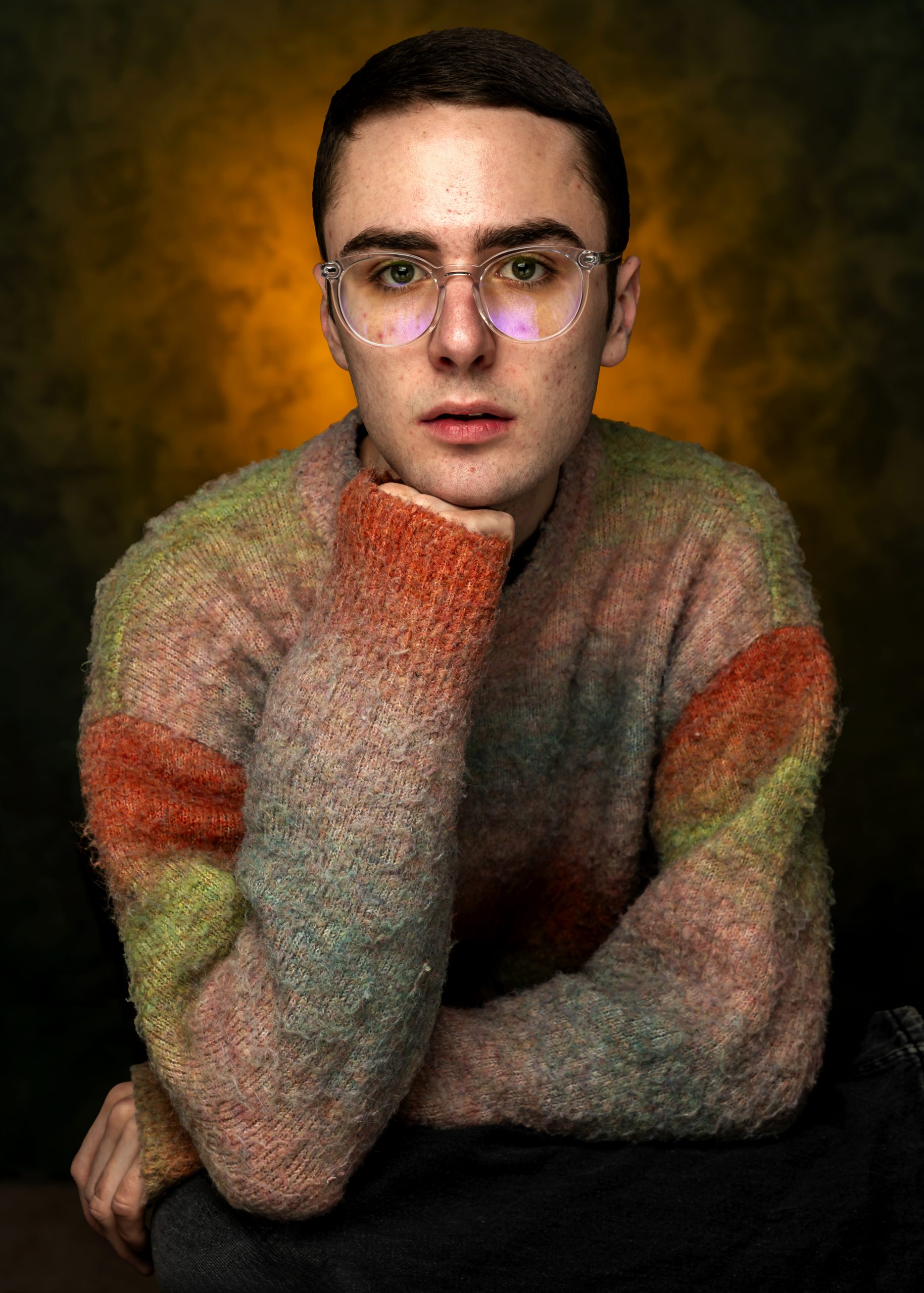 Professional creative portrait of a person in a soft multicolored sweater against a dark background, taken by Marcos Appelt Portrait Photographer in Bristol and Southwest.