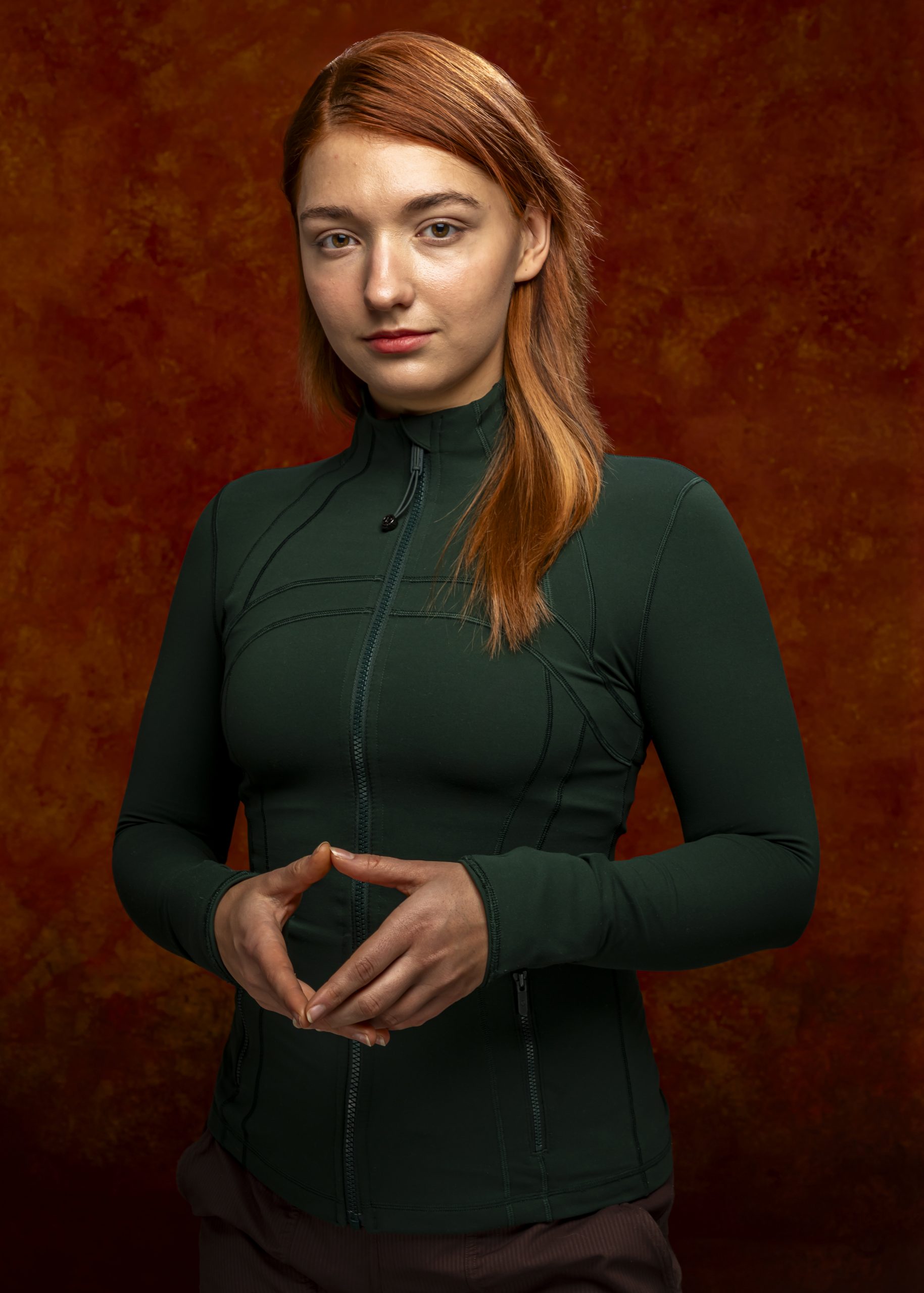 Professional portrait of a woman standing against a warm orange-brown background, taken by Marcos Appelt Portrait Photographer in Bristol and Southwest.