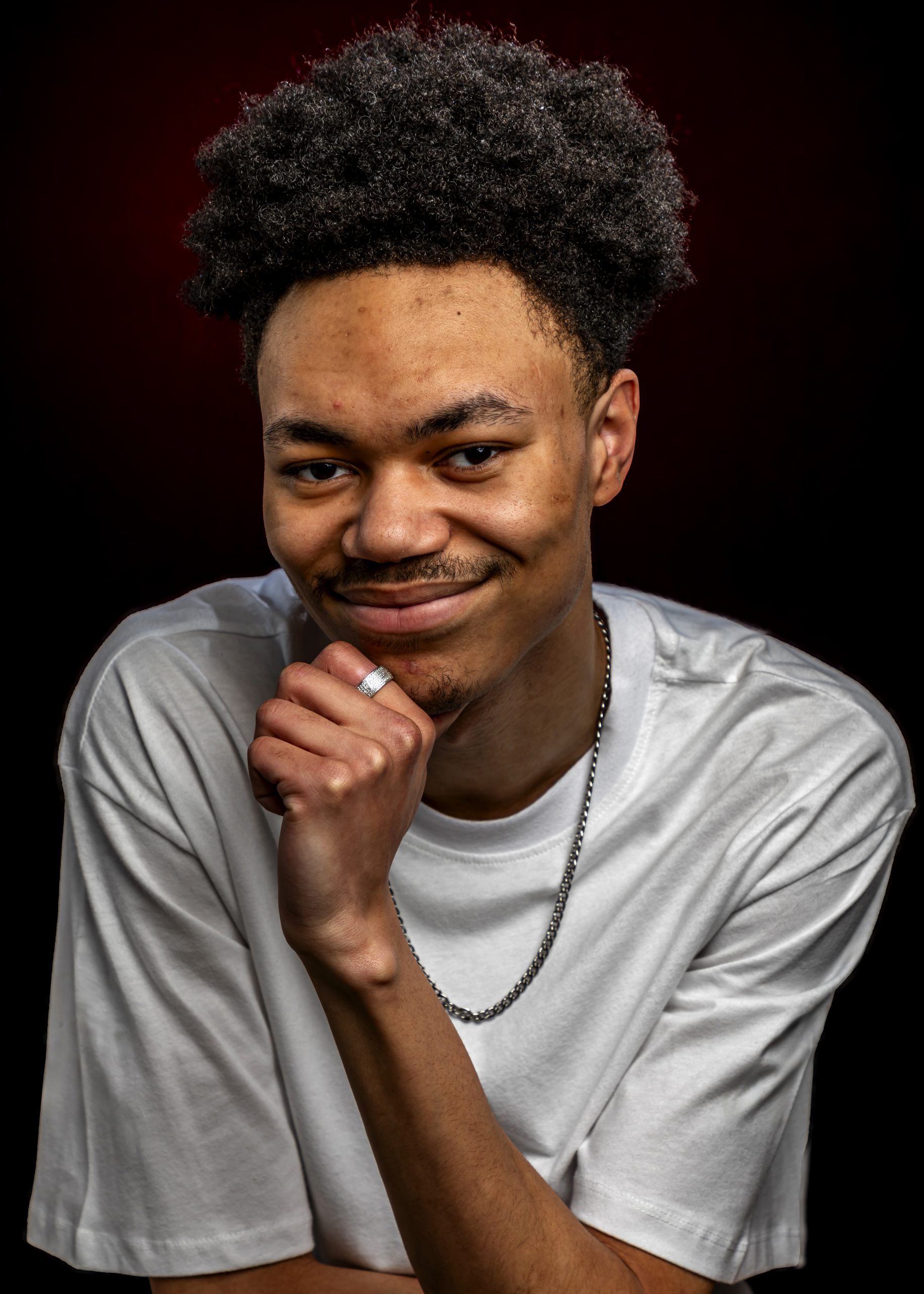 Professional headshot of a man posing thoughtfully against a red studio background, taken by Marcos Appelt Portrait Photographer in Bristol and Southwest.