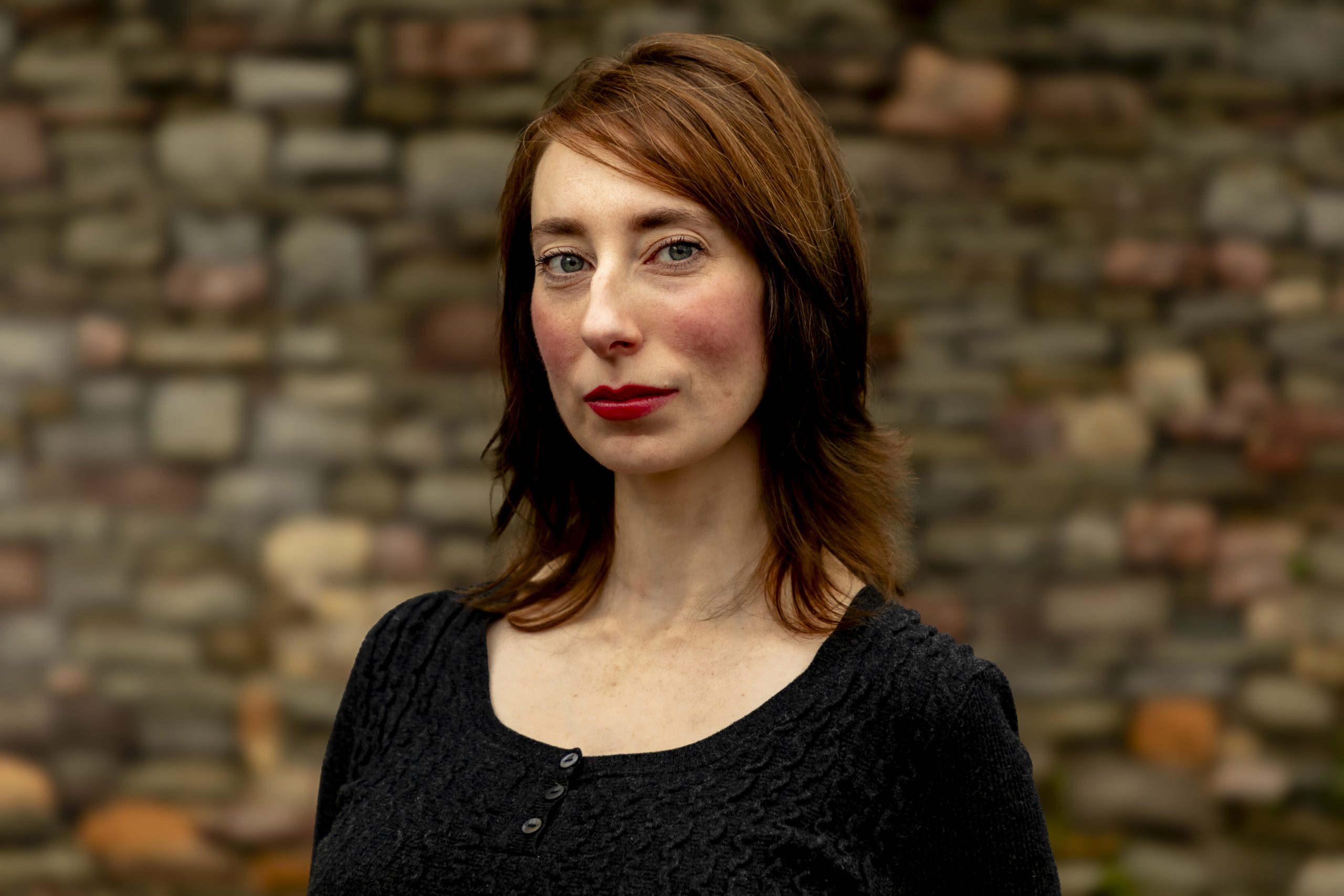 Outdoor portrait of a woman standing in front of a stone wall, taken by Marcos Appelt Portrait Photographer in Bristol and Southwest.