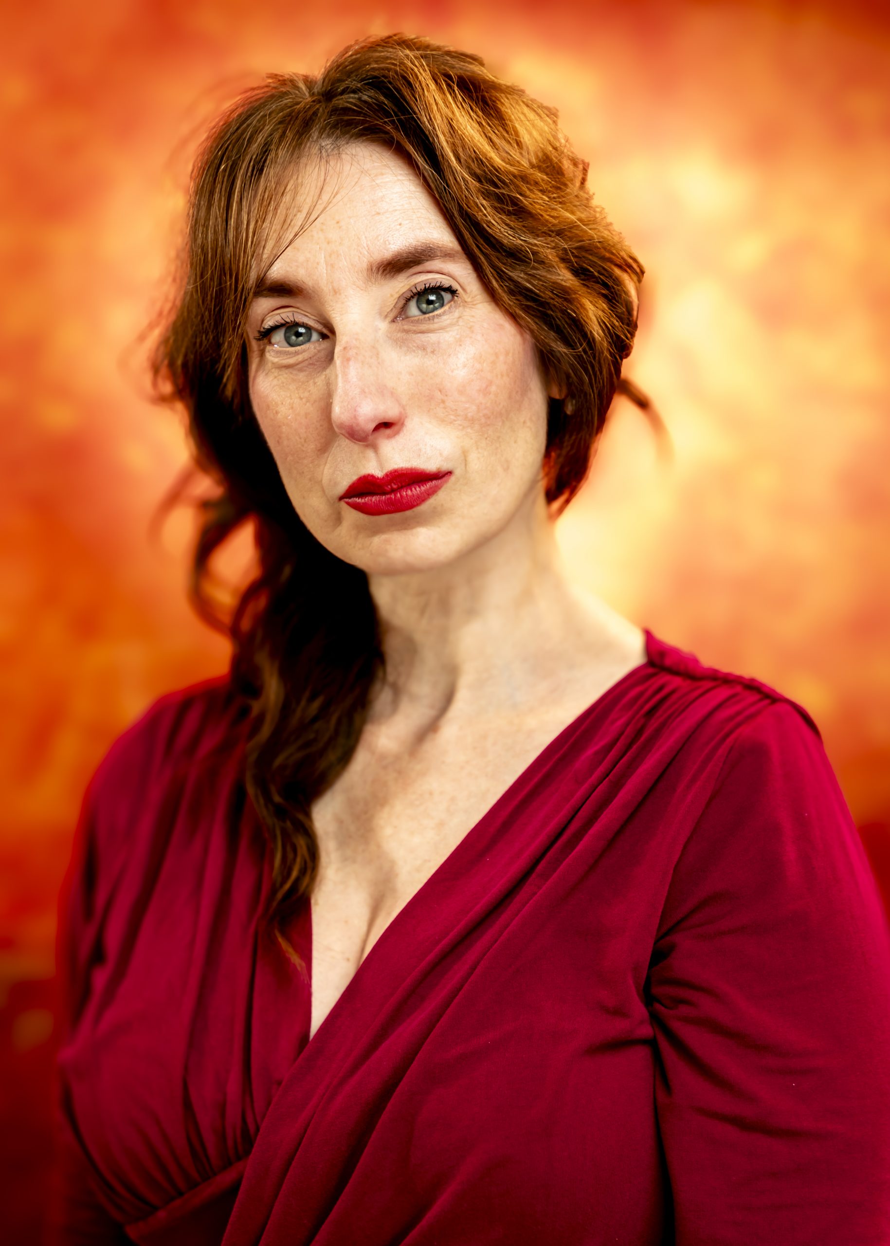 Professional portrait of a woman in a red dress against a glowing orange background, taken by Marcos Appelt Portrait Photographer in Bristol and Southwest.”