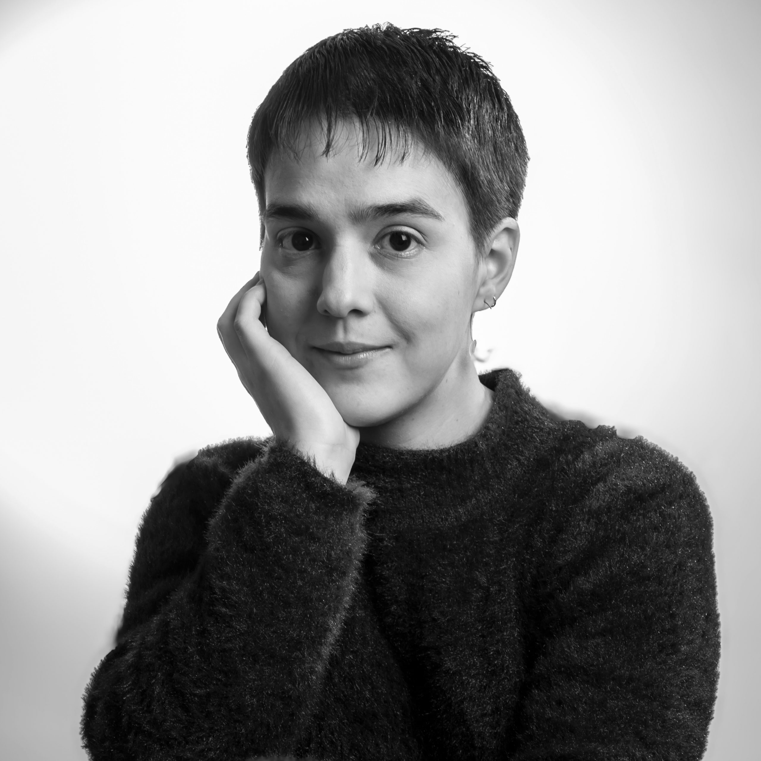 Black-and-white circular portrait of a person with short hair, resting their hand on their chin and smiling softly. Positioned next to text that reads ‘Ariadna Ortiz Naya’ and a short testimonial excerpt.