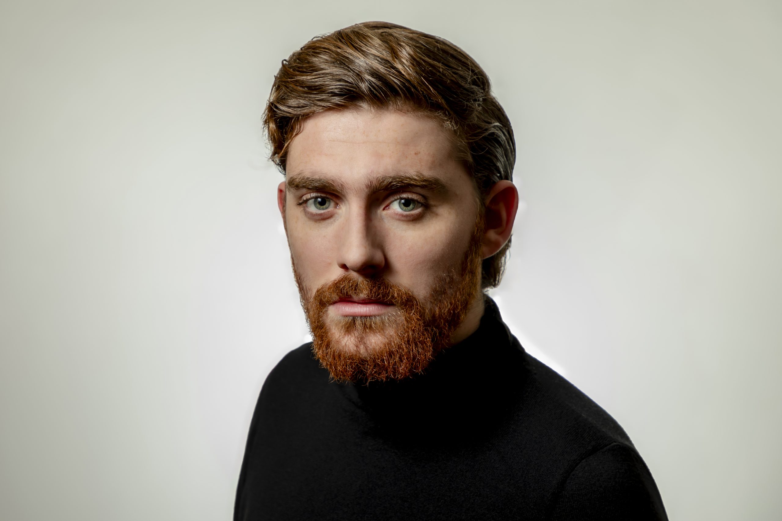 Studio portrait of a man with a beard wearing a black turtleneck against a light background, taken by Marcos Appelt Portrait Photographer in Bristol and Southwest.